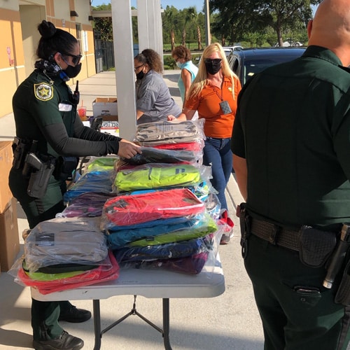 Police woman in a black uniform sorting through a table filled with unopened plastic bags of backpacks